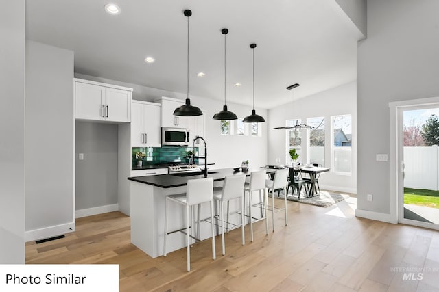 kitchen with light wood-type flooring, a breakfast bar, stainless steel microwave, white cabinets, and decorative backsplash