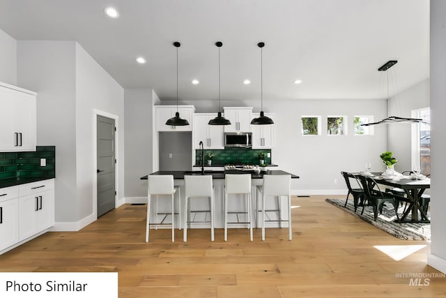 kitchen with light wood-type flooring, stainless steel microwave, a kitchen bar, and dark countertops