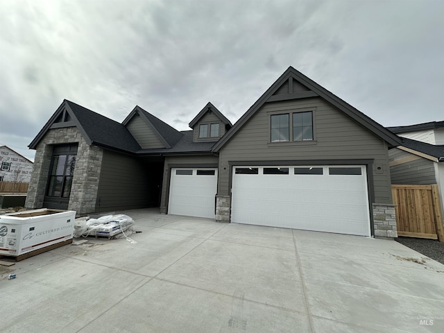 view of front of house featuring an attached garage, fence, stone siding, and driveway