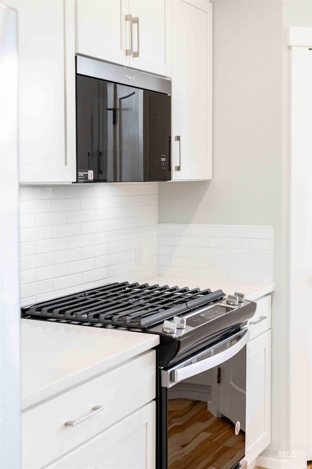 kitchen featuring black range with gas cooktop, stainless steel microwave, white cabinets, and decorative backsplash