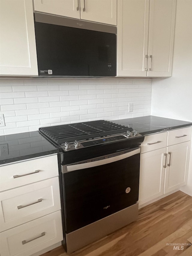 kitchen with tasteful backsplash, white cabinets, range with gas stovetop, stainless steel microwave, and light wood-style floors