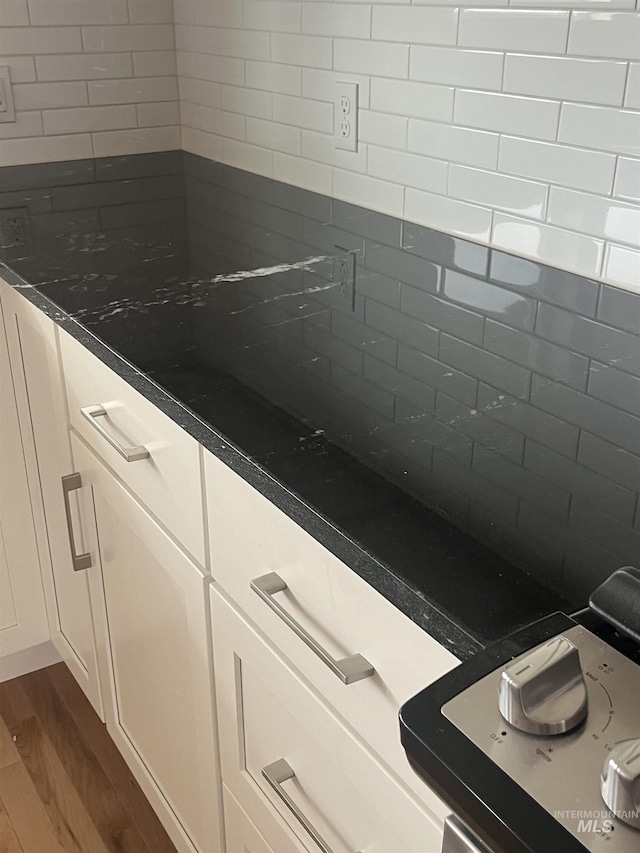 interior details with dark countertops, tasteful backsplash, white cabinetry, and dark wood-type flooring