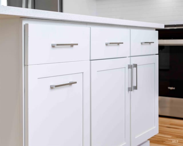 interior details with light wood-style floors, white cabinetry, and light stone counters