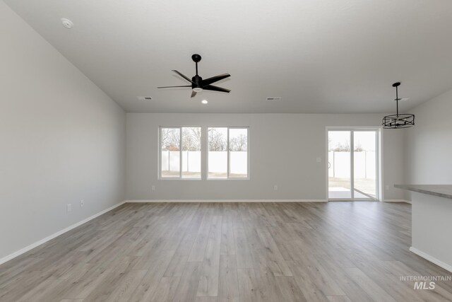 unfurnished living room featuring ceiling fan with notable chandelier, visible vents, light wood-style floors, and baseboards