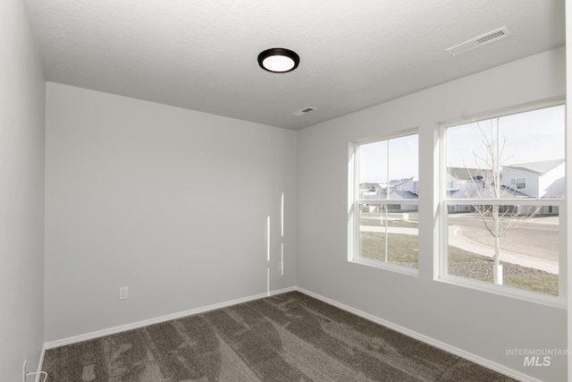 unfurnished room with dark colored carpet, visible vents, baseboards, and a textured ceiling