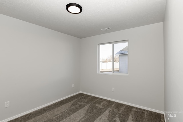 spare room with visible vents, dark carpet, a textured ceiling, and baseboards