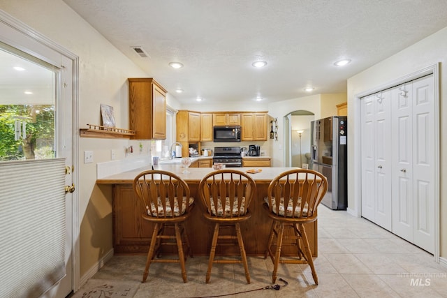 kitchen featuring a breakfast bar, light tile patterned floors, a textured ceiling, kitchen peninsula, and stainless steel appliances