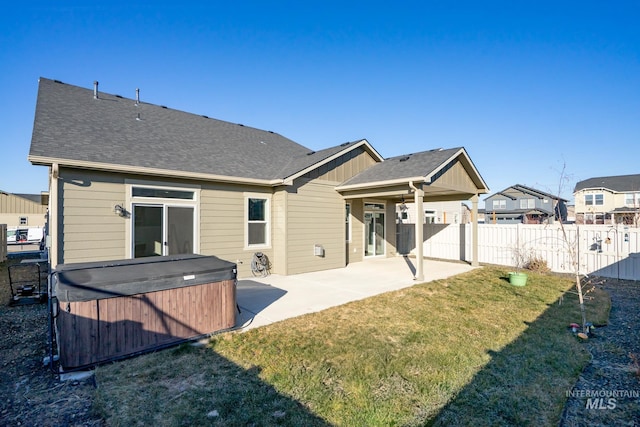 rear view of property with a hot tub, a patio, and a lawn