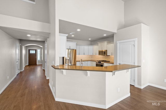 kitchen featuring white cabinetry, a kitchen bar, a high ceiling, kitchen peninsula, and stainless steel appliances