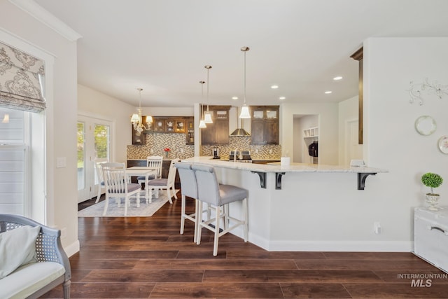 12371 S Abbott Downing Way, Nampa, ID 83686 - kitchen featuring wall chimney range hood, dark wood-style flooring, a kitchen breakfast bar, backsplash, and glass insert cabinets