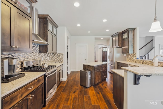 12371 S Abbott Downing Way, Nampa, ID 83686 - kitchen with dark wood-style flooring, light stone countertops, wall chimney exhaust hood, stainless steel appliances, and tasteful backsplash