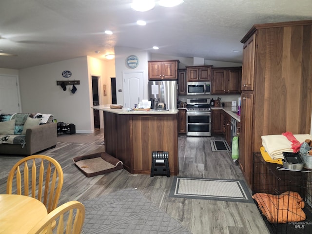 kitchen with lofted ceiling, a kitchen island with sink, dark hardwood / wood-style floors, appliances with stainless steel finishes, and dark brown cabinetry