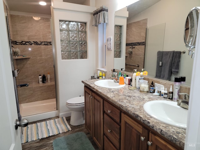 bathroom featuring a tile shower, hardwood / wood-style floors, vanity, and toilet