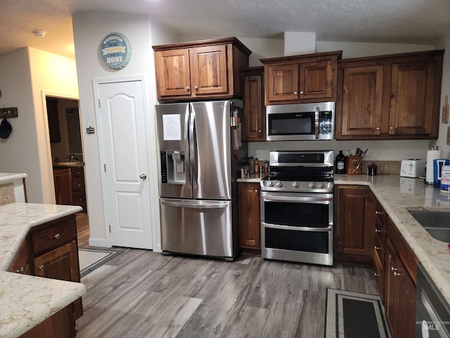 kitchen featuring light stone countertops, a textured ceiling, vaulted ceiling, appliances with stainless steel finishes, and light wood-type flooring