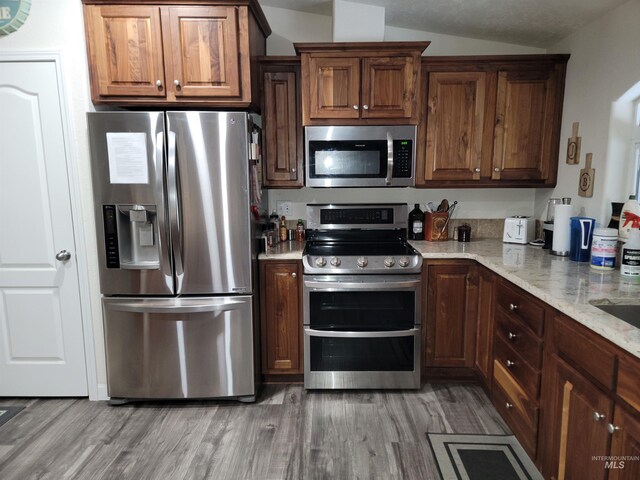 kitchen with light stone countertops, light hardwood / wood-style floors, lofted ceiling, and appliances with stainless steel finishes