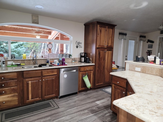 kitchen with dishwasher, light hardwood / wood-style floors, light stone counters, and sink