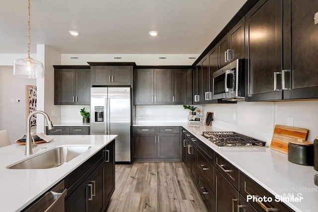 kitchen with sink, dark brown cabinetry, hanging light fixtures, light wood-type flooring, and stainless steel appliances