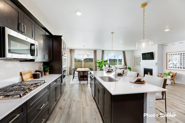 kitchen featuring a breakfast bar area, stainless steel appliances, a kitchen island with sink, decorative light fixtures, and sink