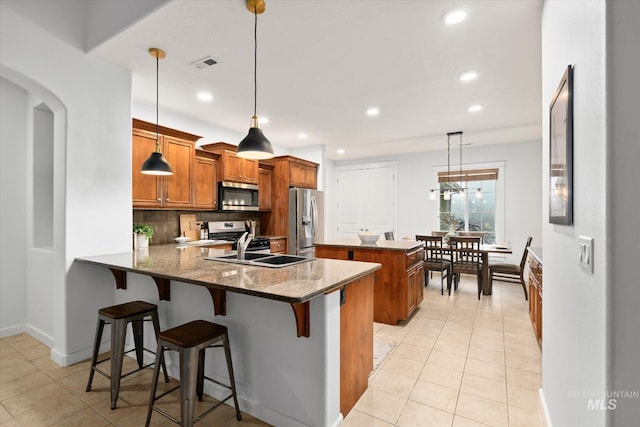 kitchen featuring appliances with stainless steel finishes, tasteful backsplash, decorative light fixtures, light tile patterned flooring, and kitchen peninsula