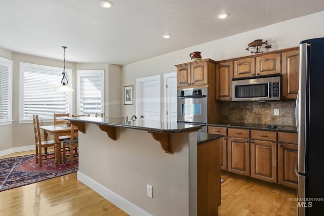 kitchen featuring stainless steel appliances, a kitchen breakfast bar, light wood-type flooring, backsplash, and brown cabinets