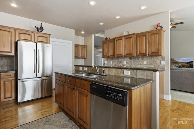 kitchen with appliances with stainless steel finishes, dark stone countertops, a sink, and light wood-style flooring