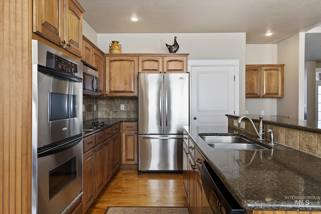 kitchen featuring light wood finished floors, decorative backsplash, brown cabinetry, black appliances, and a sink