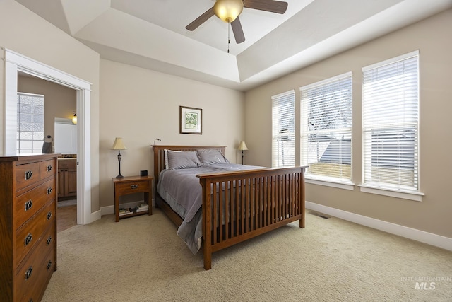 bedroom with baseboards, multiple windows, a raised ceiling, and light colored carpet