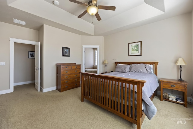 bedroom with visible vents, baseboards, light colored carpet, ceiling fan, and a tray ceiling