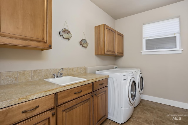 laundry area featuring washing machine and dryer, dark tile patterned flooring, a sink, baseboards, and cabinet space