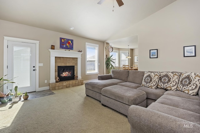 carpeted living room with vaulted ceiling, a tile fireplace, a ceiling fan, and baseboards