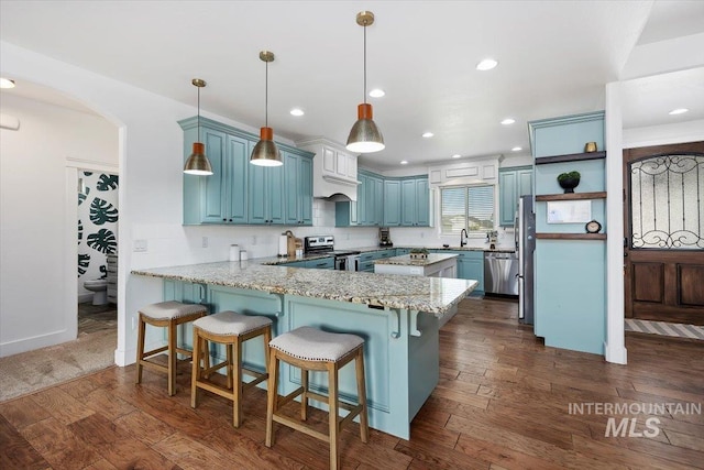 kitchen featuring dark wood finished floors, open shelves, hanging light fixtures, appliances with stainless steel finishes, and a peninsula