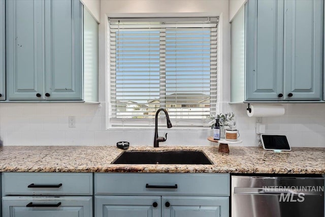 kitchen featuring decorative backsplash, light stone counters, stainless steel dishwasher, blue cabinetry, and a sink