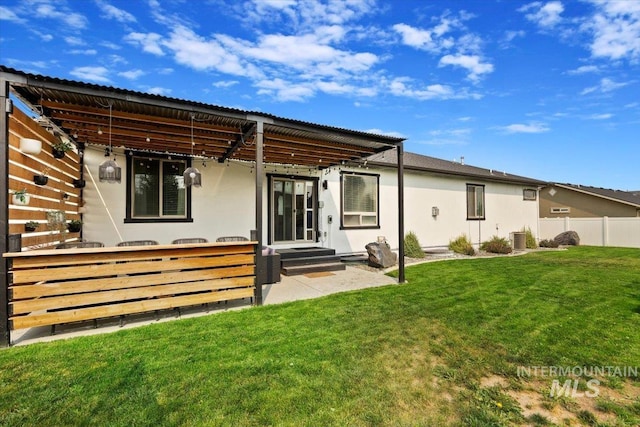 rear view of property with stucco siding, a lawn, a patio area, central AC, and fence