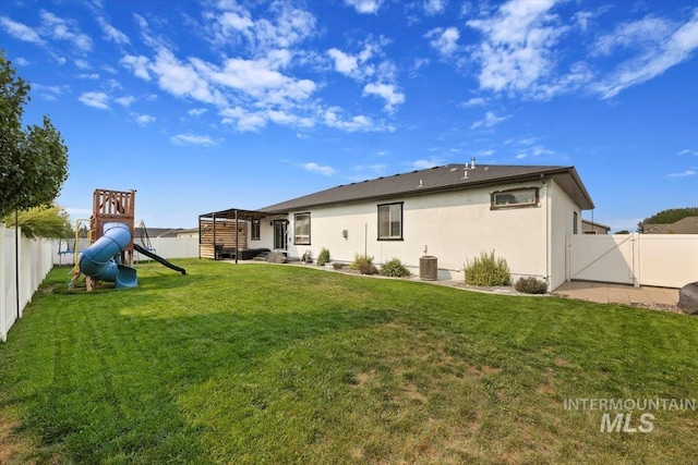 rear view of property featuring a fenced backyard, a yard, a playground, central AC, and stucco siding