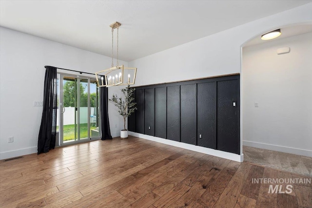 unfurnished room with an inviting chandelier, visible vents, baseboards, and wood finished floors