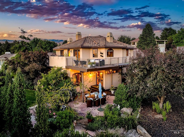 back house at dusk with a balcony, an outdoor living space, and a patio