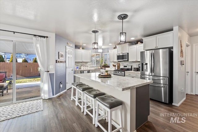 kitchen with tasteful backsplash, a breakfast bar, hanging light fixtures, appliances with stainless steel finishes, and white cabinets