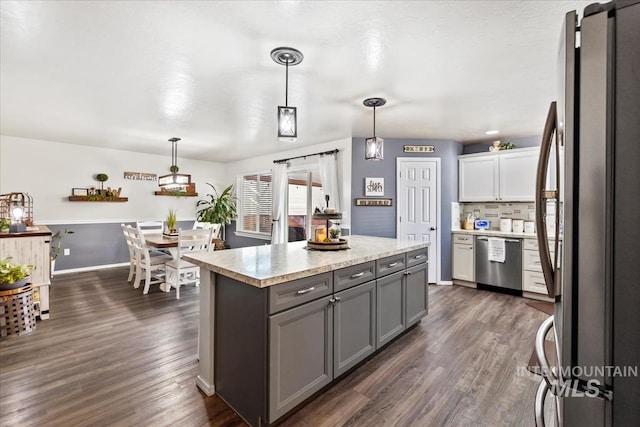 kitchen with appliances with stainless steel finishes, backsplash, white cabinetry, and decorative light fixtures