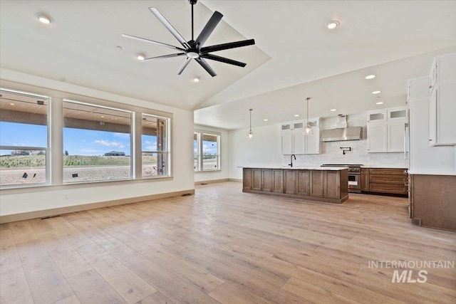 kitchen with wall chimney range hood, vaulted ceiling, white cabinetry, and open floor plan