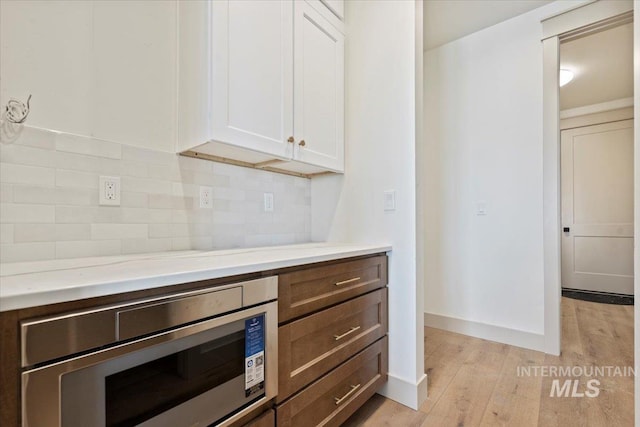 kitchen with white cabinets, stainless steel microwave, backsplash, and light wood-type flooring