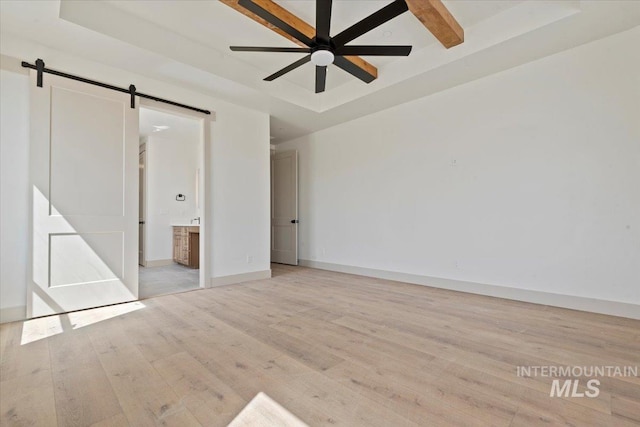 unfurnished bedroom with a barn door, light wood finished floors, baseboards, ensuite bathroom, and a tray ceiling