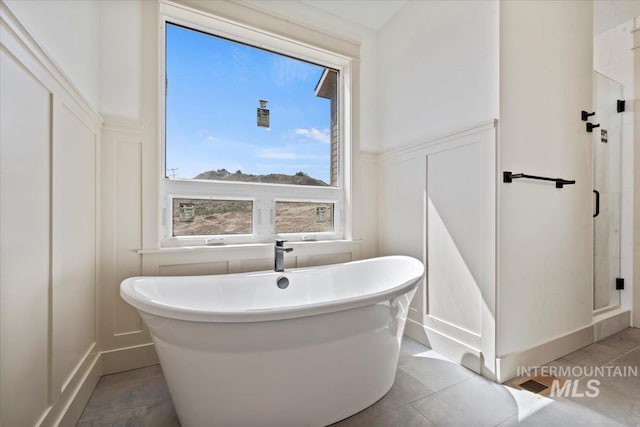 bathroom featuring a wainscoted wall, a stall shower, a decorative wall, and a soaking tub