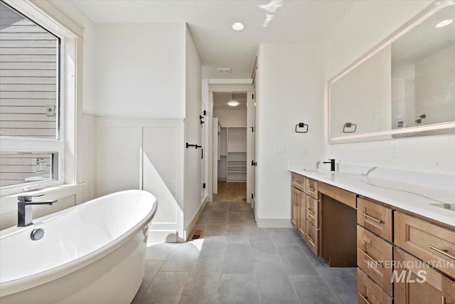 full bathroom with double vanity, wainscoting, recessed lighting, a freestanding bath, and a sink