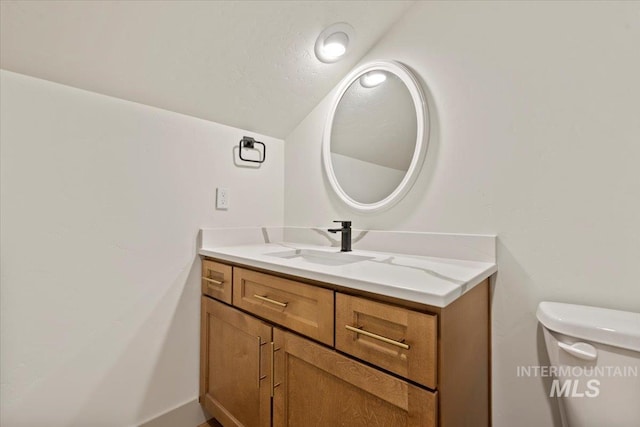 bathroom featuring vanity, toilet, and lofted ceiling