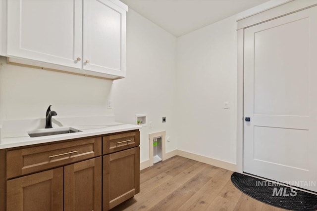clothes washing area with light wood-style flooring, hookup for an electric dryer, a sink, cabinet space, and washer hookup