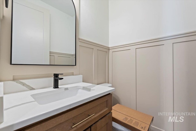 bathroom featuring wainscoting, vanity, a decorative wall, and toilet