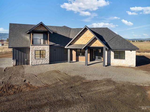 modern farmhouse featuring board and batten siding, a balcony, stone siding, and roof with shingles