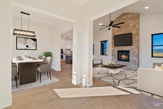 living area with wood finished floors, visible vents, a ceiling fan, high vaulted ceiling, and a fireplace