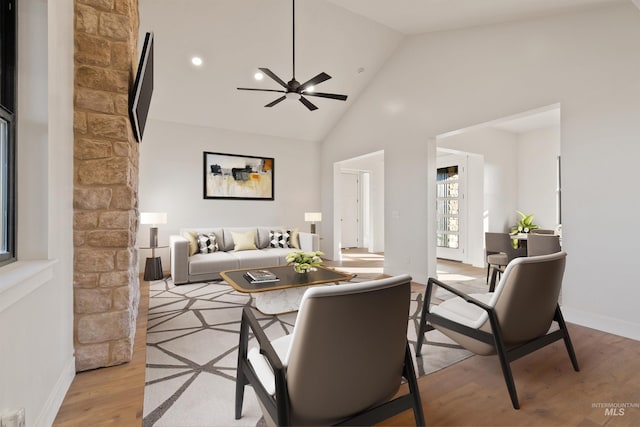 living area with a ceiling fan, light wood-style floors, baseboards, and high vaulted ceiling
