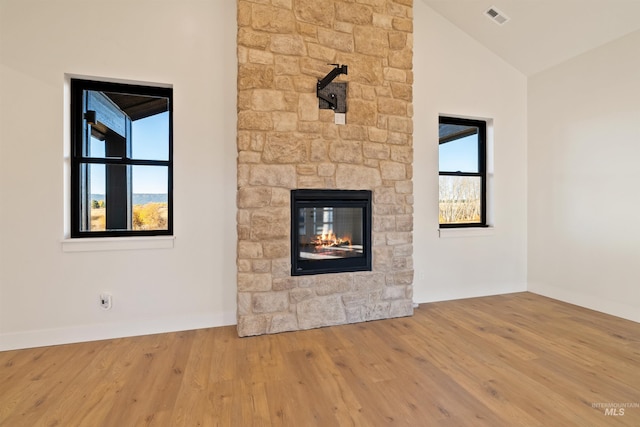 unfurnished living room with visible vents, a stone fireplace, wood finished floors, and vaulted ceiling